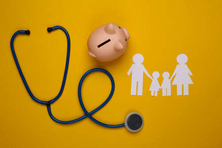 Stethoscope, paper chain family, piggy bank on yellow background, health insurance conceptの写真素材