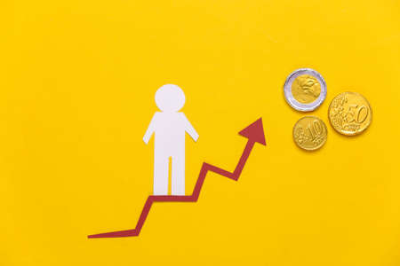 Paper man on growth arrow, coins. Yellow background. Symbol of financial and social success,...
