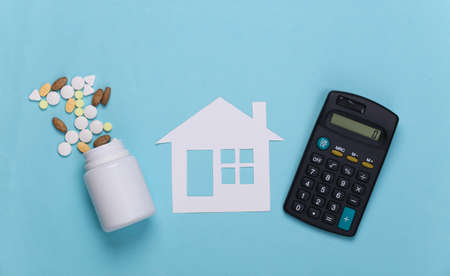 Paper house, bottle pills and calculator on blue background, health insurance conceptの写真素材