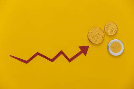 Red growth arrow and coins on yellow background. Arrow graph going up. The economic growth