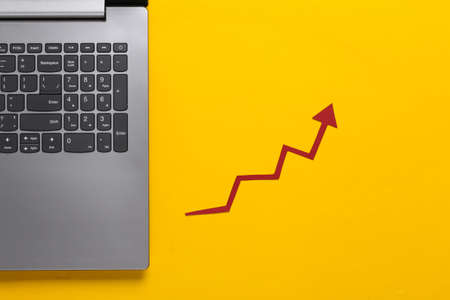 Online business, trading. Laptop and with red growth arrow on yellow background. Arrow graph going...