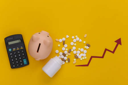 Bottle of pills with arrow tending up, piggy bank with calculator on yellow background. Top viewの写真素材