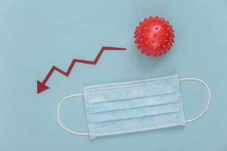 Medical facial mask and model of virus strain with falling arrow tending downwards on a blue background. Top viewの写真素材