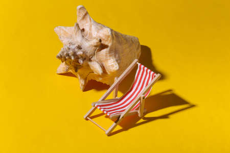 Mini beach deck chair and seashell on yellow background with shadow. Sunlight. Symbol of beach holidays, resort. Relax, Summer minimal concept.の写真素材