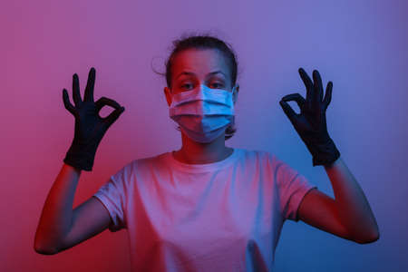 Everything's under control. Relaxed woman in medical mask and gloves shows okay symbol. Red-blue gradient neon lightの写真素材
