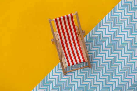 Striped mini beach deck chair on yellow blue background. Symbol of beach holidays, resort.  Relax, Summer minimal conceptの写真素材