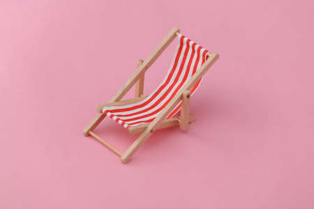 Red and white striped mini beach deck chair on pink background. Symbol of beach holidays, resort. ...