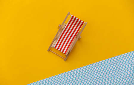 Striped mini beach deck chair on yellow blue background. Symbol of beach holidays, resort.  Relax,...