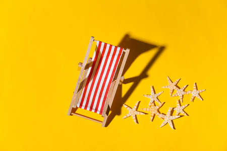 Mini beach deck chair and starfish on yellow background with shadow. Sunlight. Symbol of beach holidays, resort. Relax, Summer minimal concept. Top viewの写真素材