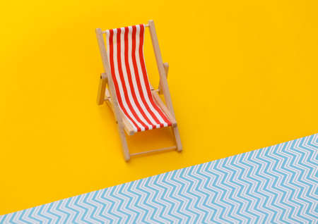 Striped mini beach deck chair on yellow blue background. Symbol of beach holidays, resort. Relax, Summer minimal conceptの写真素材