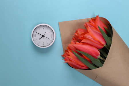 White clock and bouquet of red tulips on a blue background. Top viewの写真素材