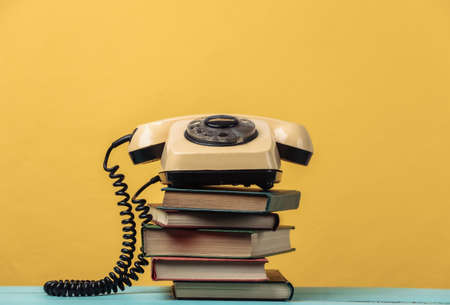 Rotary telephone on a stack of books. Yellow backgroundの写真素材
