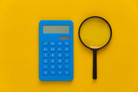Calculator with a magnifier on yellow background. Top viewの写真素材