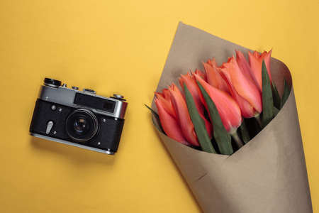 Travel concept. Bouquet of tulips and camera on a yellow background. Top view
