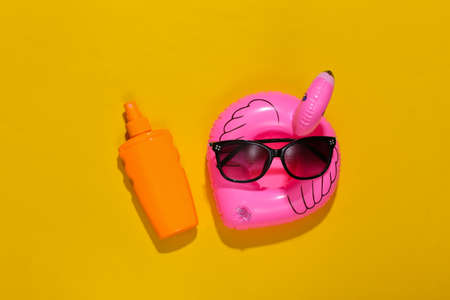beach holidays. Inflatable flamingo and sunblock bottle, sunglasses on bright yellow background. top view. minimalismの写真素材