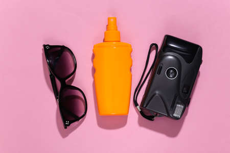 Beach vacation, travel concept. Sunblock bottle, sunglasses and camera on pink bright sunny...