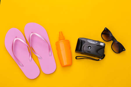 Beach vacation, travel concept. Sunblock bottle, sunglasses, flip flops and camera on yellow background. top view. flat layの写真素材