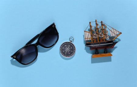 Ship figurine, sunglasses and compass on a blue bright background. Travel adventure theme. top viewの写真素材