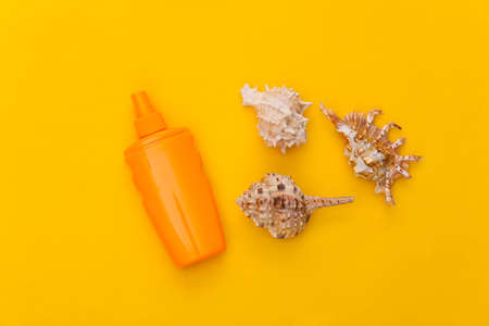 Sunblock bottle and seashell on a yellow background. skin protection. beach holidays. top view