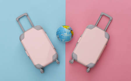 Two toy travel luggage and globe on pink blue pastel background. travel planning. top view. flat layの写真素材