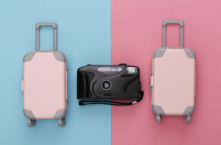 Two toy travel luggage and camera on pink blue pastel background. travel planning. top view. flat...