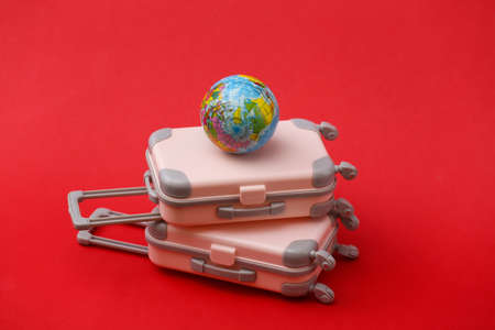 Two mini travel luggage suitcase and globe on red background. Travel still life, vacation or tourism concept.の写真素材