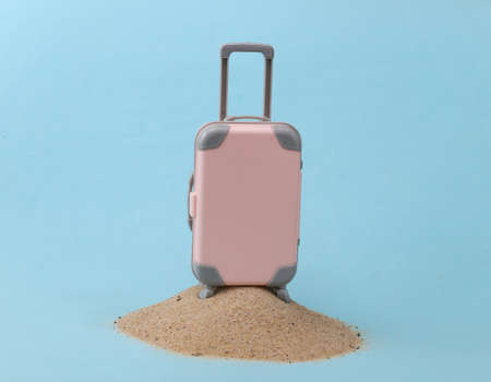 Mini travel luggage suitcase on a sand island. Studio conceptual shot. Travel, beach vacation...