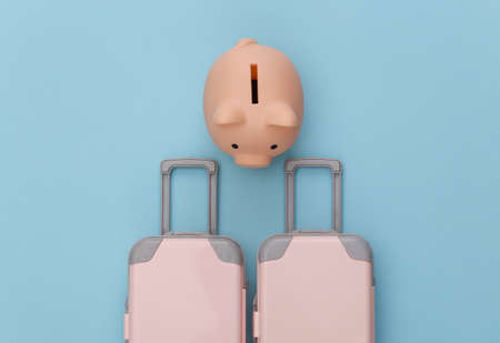 travel planning. Two toy travel luggage and piggy bank on blue pastel background. top view. flat layの写真素材