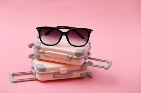 Two mini travel luggage suitcase and sunglasses on pink background. Travel still life, vacation or tourism concept.の写真素材