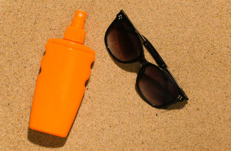 Sunblock bottle and sunglasses on the sand on bright sunny day. Beach Vacation Concept
