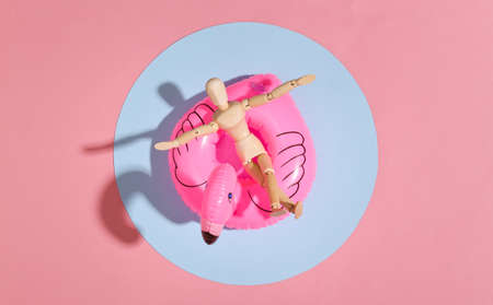 Puppet mannequin with inflatable flamingo on pink blue bright background. Beach vacation concept....