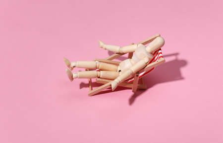 Puppet mannequin sunbathes on the deck beach chair. pink studio background. Bright sunny light. Beach Vacation Concept. summer restの写真素材