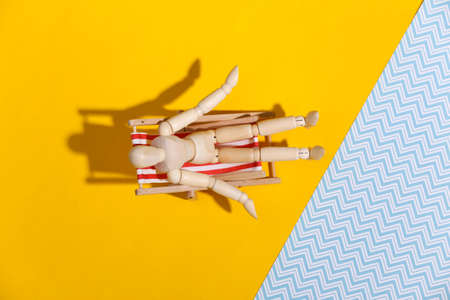 Puppet mannequin sunbathes on the deck beach chair. Yellow blue studio background. Bright sunny...