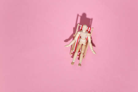Puppet mannequin sunbathes on the deck beach chair. pink studio background. Bright sunny light. Beach Vacation Concept. Summer rest. top viewの写真素材