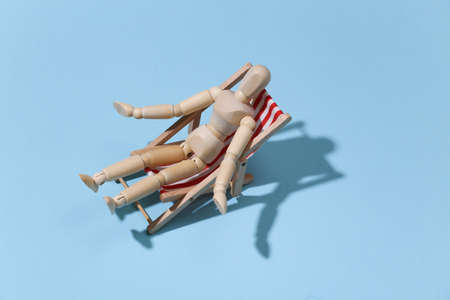 Puppet mannequin sunbathes on the deck beach chair. blue studio background. Bright sunny light. Beach Vacation Concept. summer restの写真素材