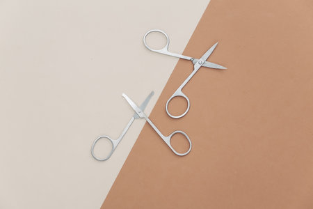 Two pairs of nail scissors on a beige-brown background. top view
