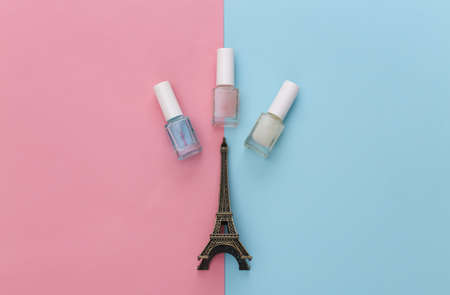 Nail polish and statuette of Eiffel tower on pink blue background. beauty concept. top viewの写真素材