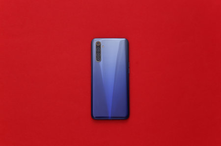 The back cover of a modern smartphone with lenses on red background with white frame. top view