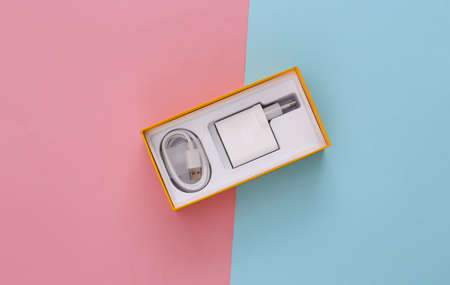 Box for a smartphone with a charger on a blue-pink pastel background. top view