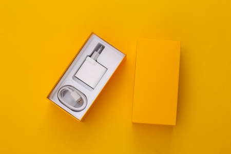 Box for a smartphone with a charger on yellow background. top view