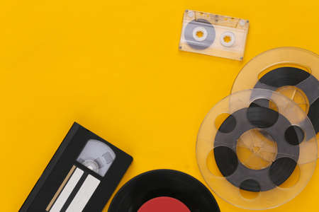 Retro flat lay. Audio magnetic tape reel, audio and video cassette, vinyl plate on yellow...