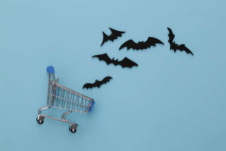 Halloween discounts, shopping. Supermarket trolley and flying bats on blue background. Halloween...