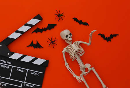 Horror movie, halloween theme. Movie clapperboard, skeleton, spiders and flying decorative bats on orange background. Top view, flat layの写真素材