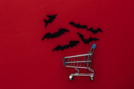 Halloween sale, shopping. Supermarket trolley and flying bats on red background. Halloween...