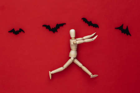 Halloween scary concept. Wooden puppet runs away on red background with flying bats