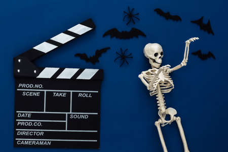 Horror movie, halloween theme. Movie clapperboard, skeleton, spiders and flying decorative bats on classic blue dark background. Top view, flat layの写真素材