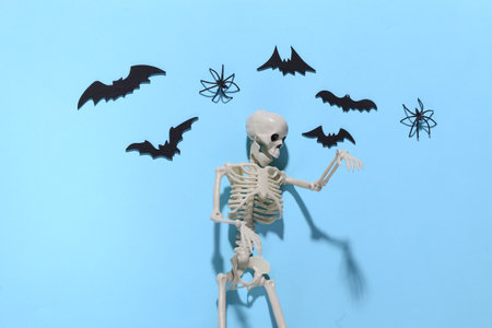 Halloween background, decorations and scary concept. Skeleton and spiders, black bats fly over blue...