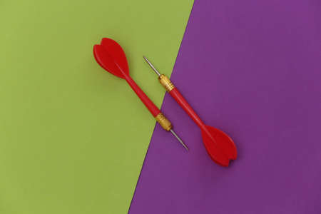 Two red plastic darts with metal tip on purple green background. top view. flat lay. minimalismの写真素材
