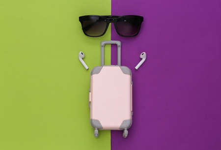 Mini travel luggage and wireless headphones, sunglasses on a purple-green background. top viewの写真素材