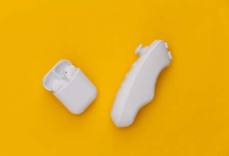 Modern joystick and wireless headphones on yellow background. top view